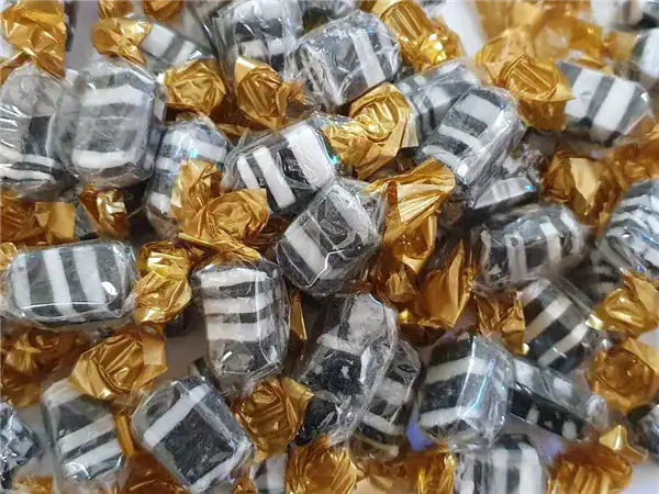 Delicious black and white striped candies wrapped in gold foil, perfect for gifting or party favors.